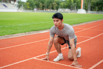 Fototapeta premium Asian man sprinter crouching getting ready at the start line of running track in sports stadium.