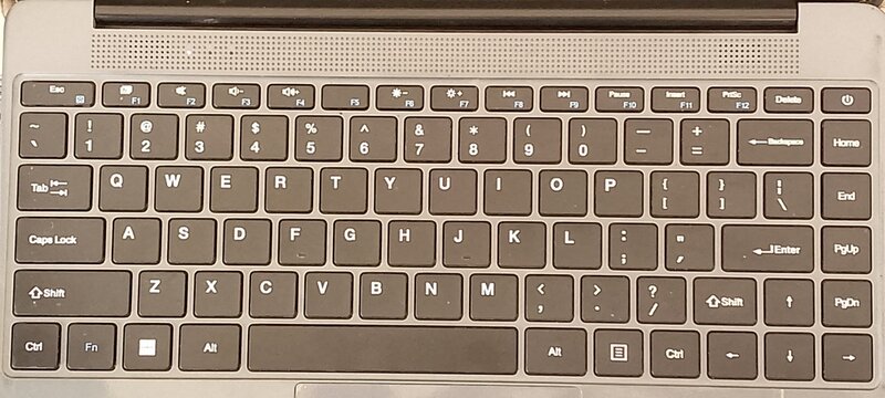 Top down view of a dark grey laptop keyboard featuring standard qwerty layout with function keys and dedicated media controls set against a neutral background for professional computing office