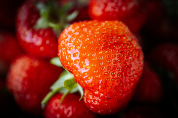 Macro view of glossy ripe strawberries piled together, featuring vivid red color, green leaves, natural texture, and shallow depth of field. © Jolanta