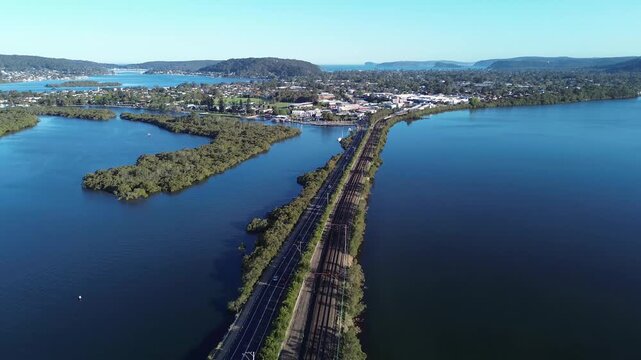 Intercity train Sydney to Newcastle. Train stop Woy Woy.Train travels alongside river with road in view during a sunny day near a forested area