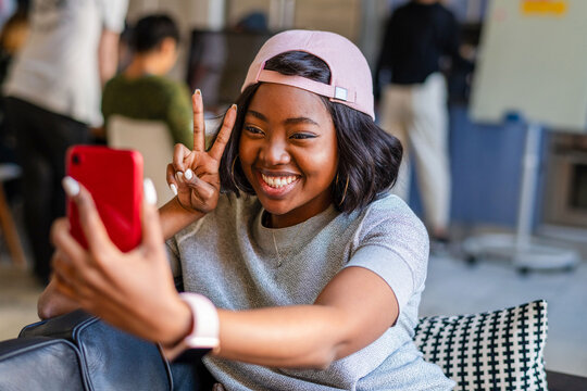 Smiling Black woman taking a selfie and flashing a peace sign indoors