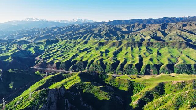 Aerial view of the winding mountain road of the S101 highway through lush green hills in Xinjiang, China.