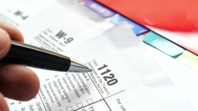 Close up of hand holding pen over tax form 1120 and w-9 document preparing to fill out forms