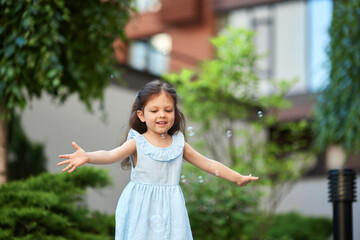 Fototapeta premium Happy little girl stretching arms catching bubbles