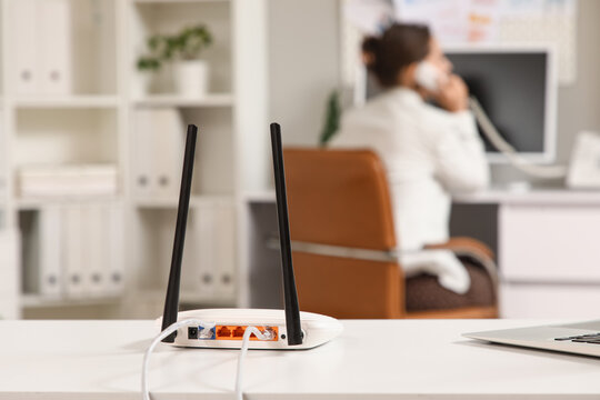 Wireless router on a white office desk with a blurred person working in the background, internet connectivity and modern workplace