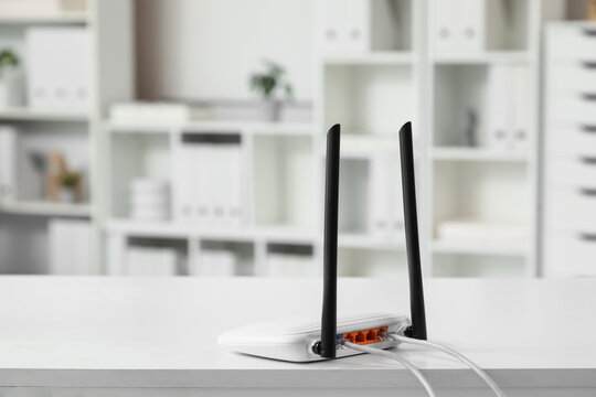 White wireless router with black antennas and connected ethernet cables on a clean white desk in a modern office, this setup provides essential internet access for home or business operations