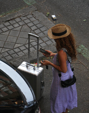 Viajera con maleta, tel&eacute;fono m&oacute;vil y sombrero en maletero coche vacaciones escapada