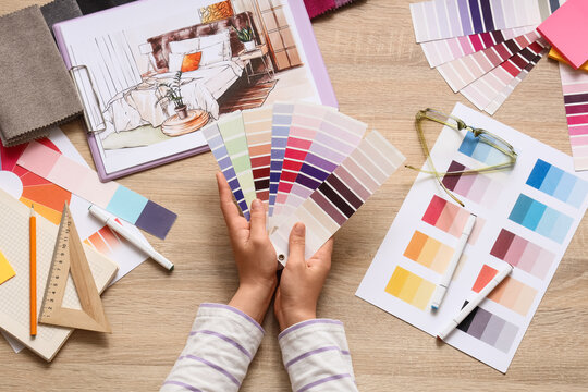 Interior designer holding color palette swatches for bedroom renovation project on wooden table, top view