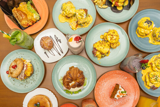 Colorful Brunch Spread Overhead: Eggs Benedict Variations, Croissant Sandwich, Pancakes, Smoothies, Muffin and Carrot Cake