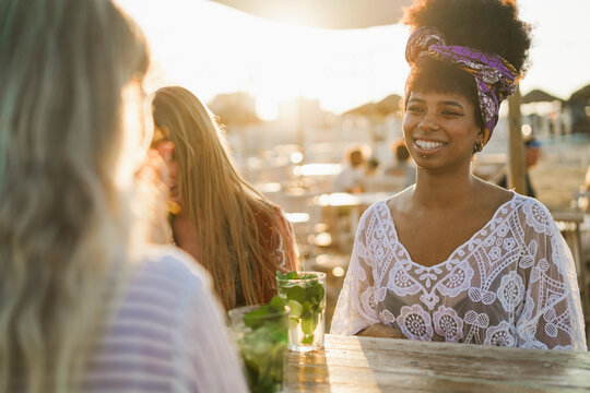 Multiracial happy women friends drinking mojitos at beach party - Summer lifestyle, travel and vacation concept - Focus on african girl face - UGC content