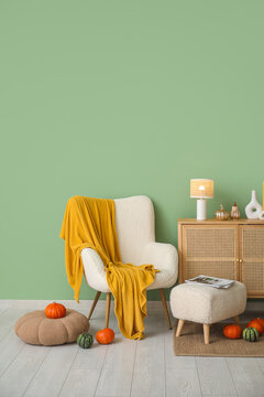 Autumn interior of living room with white armchair, lamp, pumpkins and chest of drawers