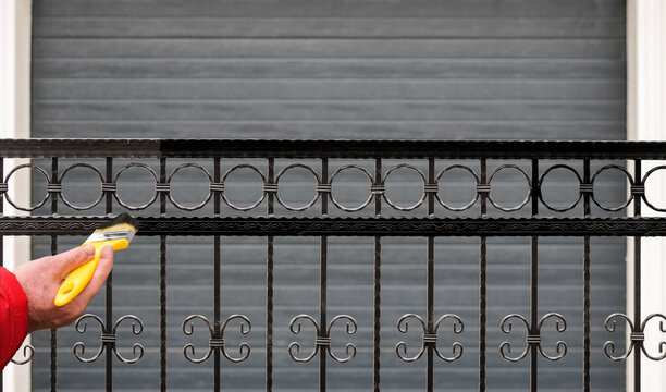 Hand Painting a Metal Fence with a Brush. Home Maintenance, Rust Protection, Renovation, and DIY Improvement Concept.
