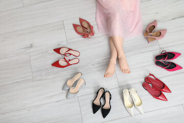 Naklejka premium Barefoot legs among variety of shoes on white wooden background
