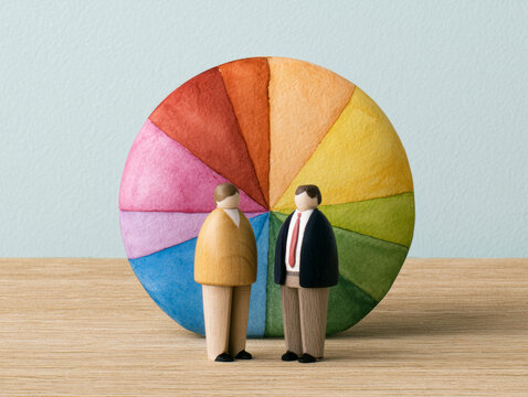 Two wooden business figures stand in front of colorful pie chart symbolizing second half business planning for year end budget planning and financial strategy discussion