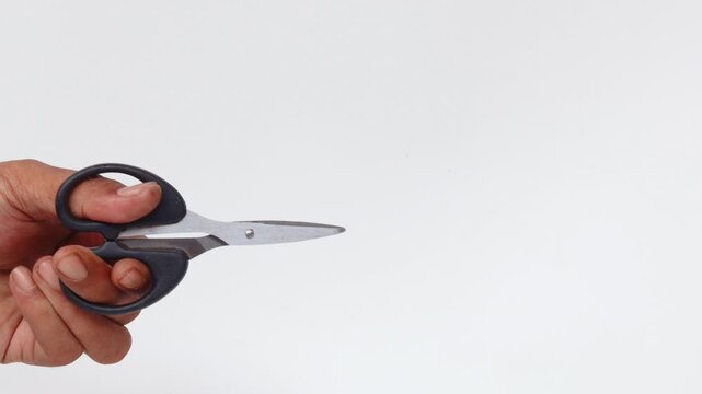 Close-up of an Asian man's hand making a cutting motion with a pair of scissors isolated on a white background.
