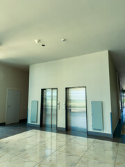 Fototapeta premium Elevators stand in a modern building hallway during daytime with grey walls and white tiles nearby a door