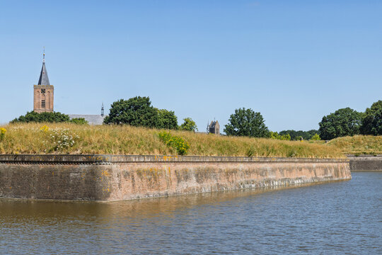 Naarden Vesting, Netherlands. Corner view of a monumental brick defensive wall in the moat water, with the Grote Kerk church tower visible in the background.