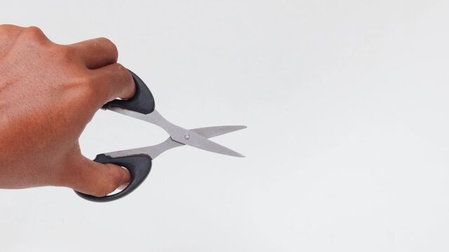 Close-up of an Asian man's hand making a cutting motion with a pair of scissors isolated on a white background.