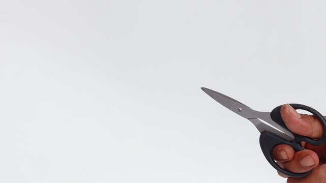 Close-up of an Asian man's hand making a cutting motion with a pair of scissors isolated on a white background.