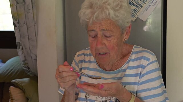 Healthy aging and active senior lifestyle elderly woman eating nuts from her hands in a home kitchen close-up shot