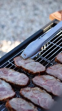 Vertical video of placing pork shoulder on grill with tongs