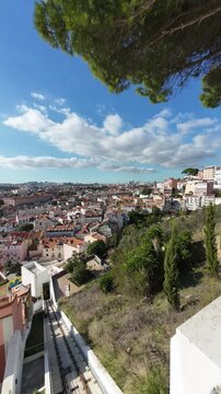 Vertical timelapse from a Lisbon viewpoint overlooking the city with a historic funicular climbing and descending a steep hillside track under a blue sky