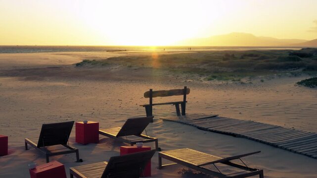 Fixed shot of empty beach stretchers, with sand blowing in the wind and sun shinning on the background, Tarifa, Andalusia, Spain