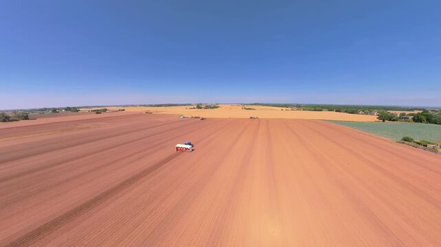 Aerial view of tractor tilling vast red earth. Farming in Lincolnshire. Farm workers planting seedlings for new summer crops