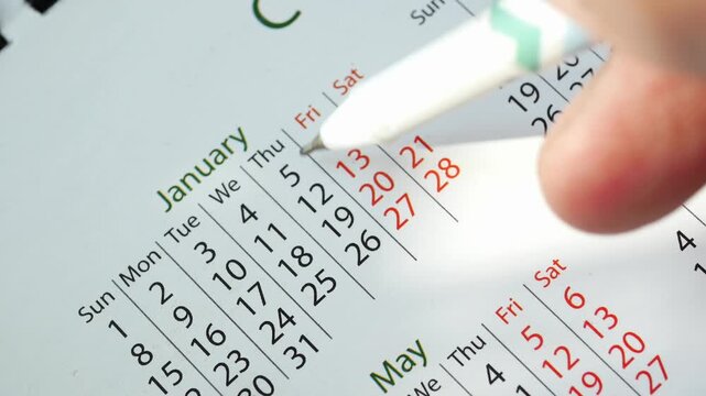 Close up video of a person hand using a white pen to circle important dates on a paper calendar, showcasing event planning and scheduling concept