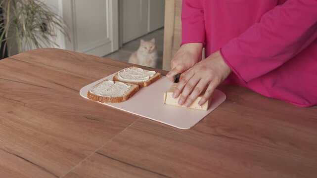A woman's hands slice cheese for sandwiches with a knife.