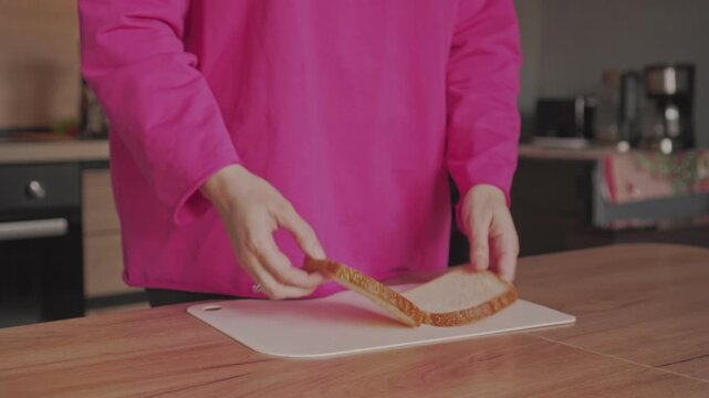The hands of a housewife woman place pieces of bread on a cutting board on the kitchen table.