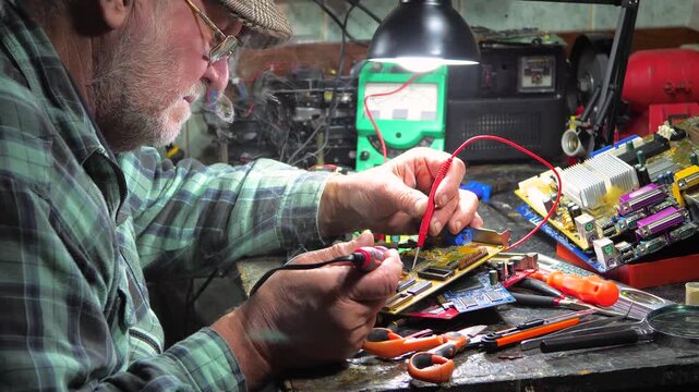 An elderly technician repairs computer equipment in a workshop using measuring instruments and technical tools. Slow motion.