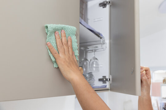 Hand cleaning kitchen carbinet door with green microfiber cloth.