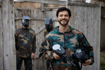 Fototapeta premium Portrait of a smiled soldier holding his weapon and a helmet with other soldiers on the background