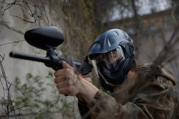 Fototapeta premium Confident soldier aims a paintball gun while hiding in the dry trees