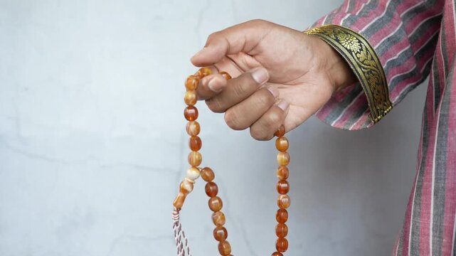 Close up shot of person hand wearing traditional attire holding prayer beads while counting the number of beads