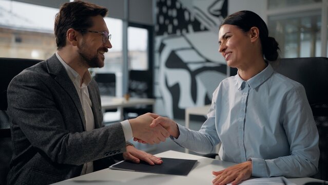 Two Caucasian partners shaking hands after conclude successful business contract trading in office businesswoman handshaking with businessman signing document at table cooperation sale trade handshake