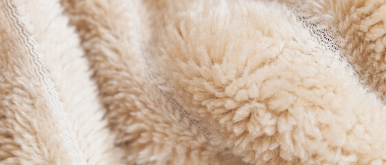 Panoramic close up of a fluffy beige sherpa fleece fabric showing soft delicate curly wool fibers on a warm cozy blanket surface with copy space © moryachka
