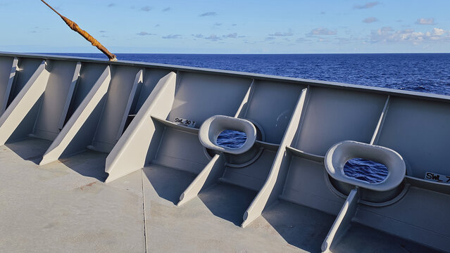 Horizontal close up of grey painted steel bulwark and mooring chocks on the deck of a commercial cargo ship sailing in the deep blue ocean during a sunny day