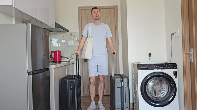 Adult man entering hotel room with rolling suitcases and looking around after arrival. Guest checking accommodation, exploring interior, travel, vacation, business trip and hotel check in concept