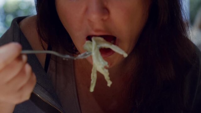 Close up of woman eating fresh salad with fork, showing mouth, enjoyment, healthy eating lifestyle in outdoor setting.
