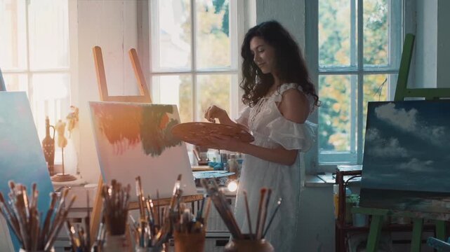 Female artist painting on canvas in bright art studio with palette and brush, Creative woman working at easel with natural sunlight inspiring artistic self expression indoors 4k