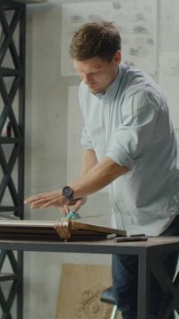 man wrapping or tying a package in an indoor office setting with metal shelving and a table, neutral focused on task, side view, white and blue colors, paper and string materials, business.