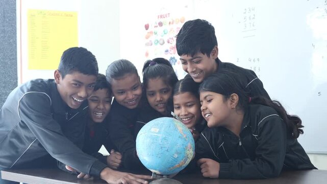 Group of indian school students observing and discussing world globe on a desk while learning geography in classroom. Knowledge and Education in india.