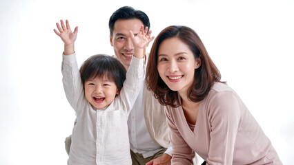 Fototapeta premium Happy Korean family portrait with joyful arms-raised toddler and smiling parents against isolated white background.