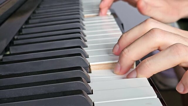 Close up video of hands playing piano keys with fingers moving across black and white keyboard, musician performing melody on piano, detailed musical performance footage