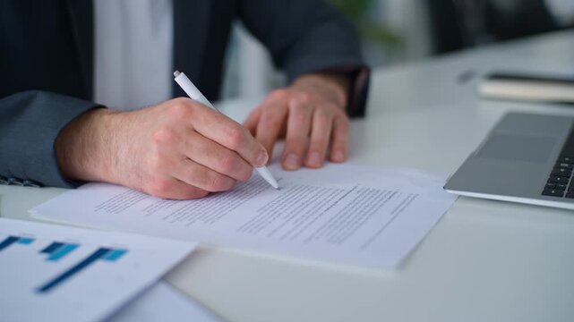 Close up male hands signing business paper approved loan mortgage trading selling contract at table in office. Unknown businessman writing signature in document conclude deal paperwork in company