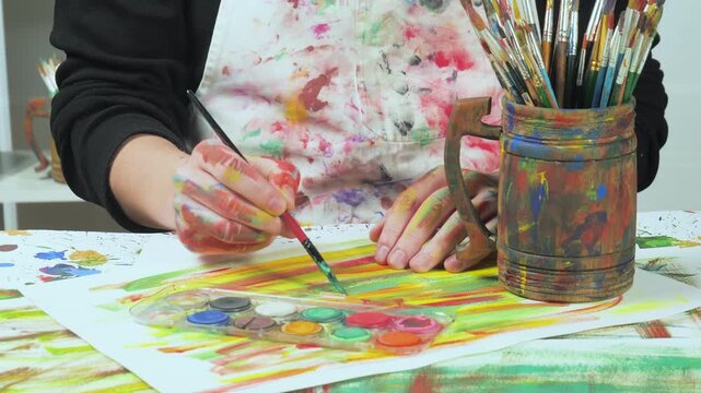 An artist applies watercolor paint to a brush. Close-up of his hands.