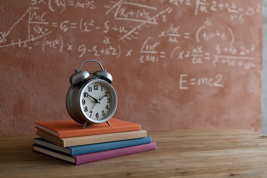 Retro metal alarm clock sitting on stacked notebooks with chalkboard formulas for classroom study background and learning poster use