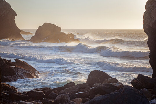 Praia da Ursa, Portugal: Ocean waves crashing against rocks at sunset